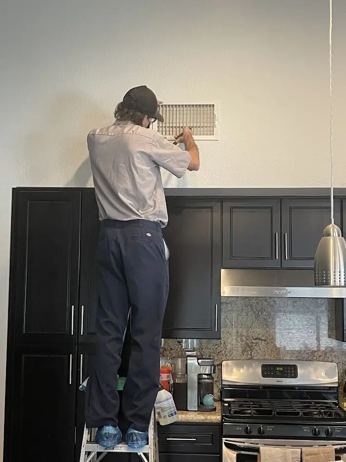 Technician inspecting an air vent during HVAC service in North Ogden